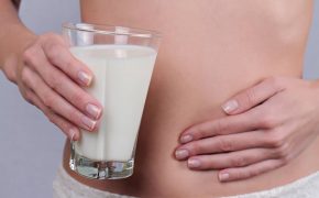 Woman with stomach pain holding a glass of milk. Dairy Intolerant person. Lactose intolerance, health care concept. Selective focus on glass of milk
